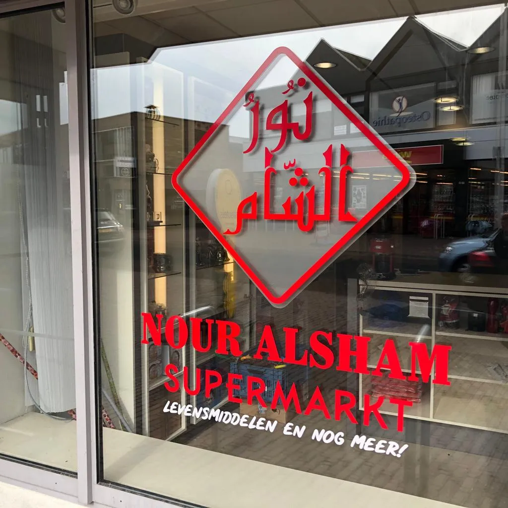 Rode raambelettering met logo voor Nour Alsham Supermarkt op de etalageruit door ZON Reclame.